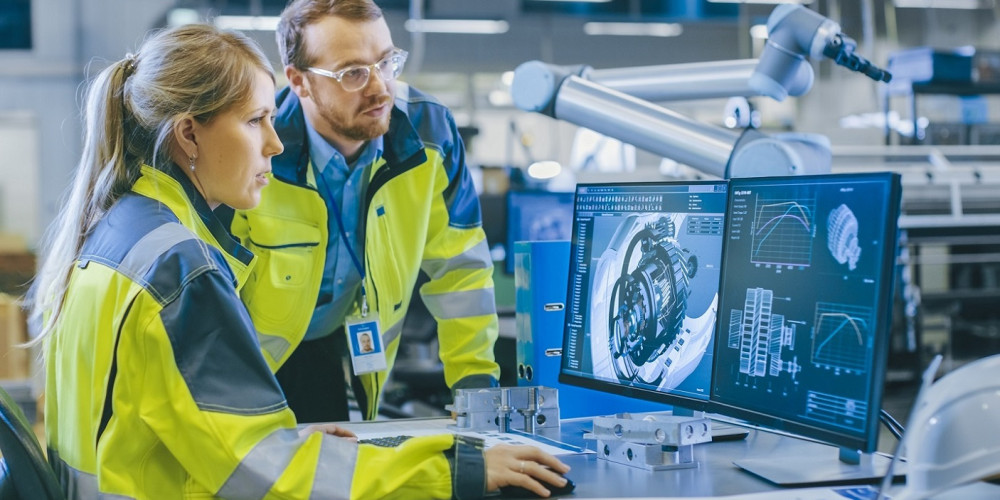 At the Factory: Male Mechanical Engineer and Female Chief Engineer Work Together on the Personal Computer, They Discuss Details of the 3D Engine Model for Robotic Arm.