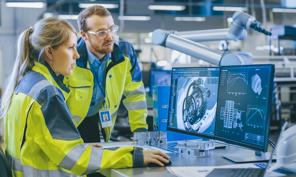 At the Factory: Male Mechanical Engineer and Female Chief Engineer Work Together on the Personal Computer, They Discuss Details of the 3D Engine Model for Robotic Arm.